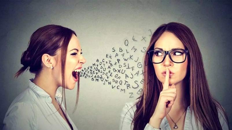 یک خانم عینک زده و دست خود را به علامت سکوت روی لبهایش قرار داده و خانم دیگری در کنار او ایستاده و در حال فریاد زدن است. 