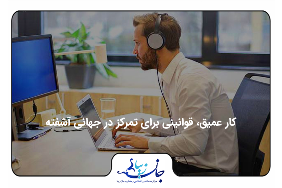 مردی پشت میز کار نشسته و هدفون به گوش دارد و در حال کار کردن با لپتاپ و نگاه کردن به مانیتور بزرگ روی میز است