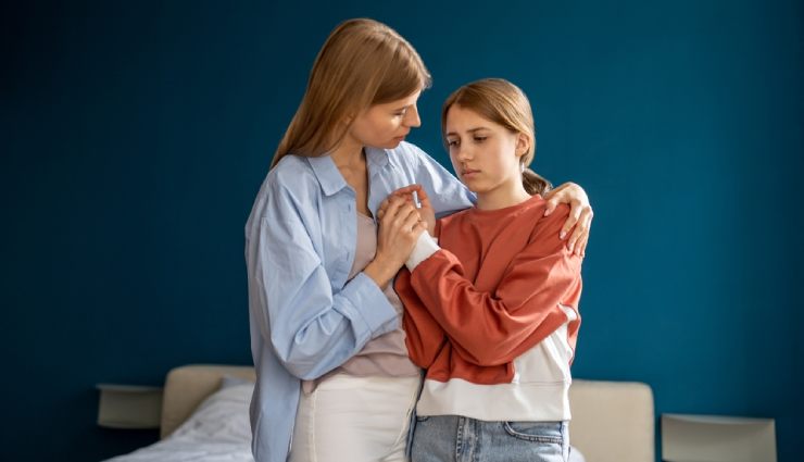 مادر و دختری کنار هم ایستاده  و مادر، دختر را در آغوش گرفته است. 