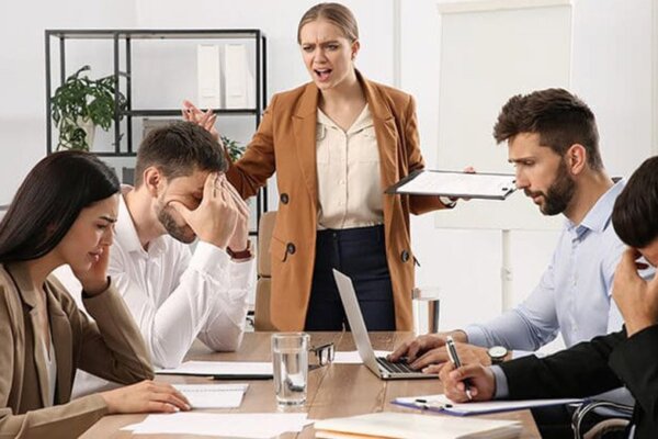 دو خانم و دو آقا با ناراحتی دور میز کار نشسته‌اند و یک خانم ایستاده و در حال فریاد زدن سر آن‌ها است.