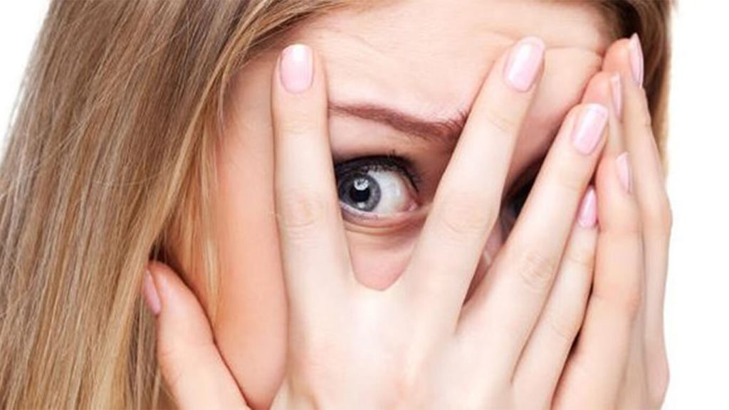 خانمی که دستش را روی صورتش قرار داده و با ترس از بین انگشتانش به نقطه‌ای نگاه می کند. 
